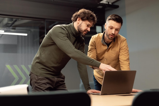 Konzentrierter Geschäftsmann, der auf einen Laptop-Bildschirm zeigt, der mit einem männlichen Kollegen an einem Geschäftsprojekt arbeitet