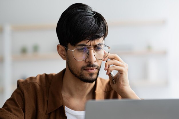 Konzentrierter indischer Manager, der am Laptop arbeitet und ein Telefongespräch führt