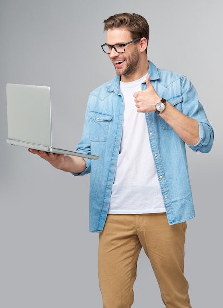 Konzentrierter junger bärtiger Mann, der eine Brille trägt, die im Jeanshemd gekleidet hält Laptop lokalisiert