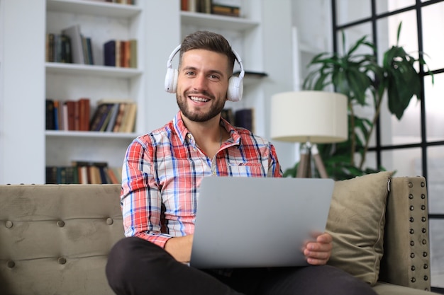 Konzentrierter junger freiberuflicher Geschäftsmann, der mit Laptop auf dem Sofa sitzt und zu Hause aus der Ferne online arbeitet.