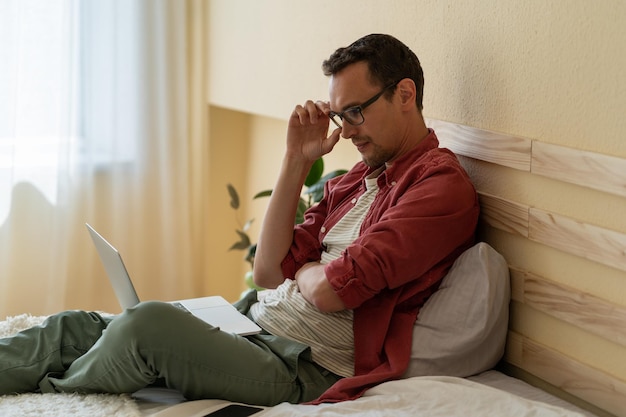 Konzentrierter kaukasischer Mann sitzt auf dem Bett im Hotelzimmer und liest Nachrichten über das Internet oder checkt E-Mails