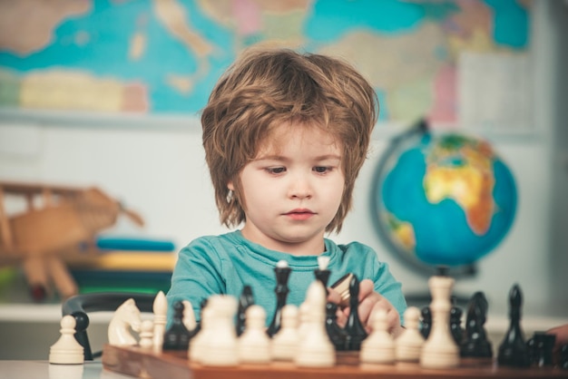 Konzentrierter kleiner Junge, der am Tisch sitzt und Schach spielt Junge, der zu Hause Schach spielt