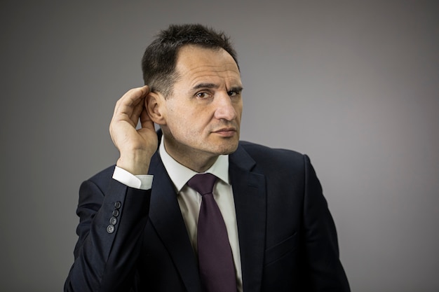 Konzentrierter männlicher Geschäftsmann mit der Hand am Ohr, der versucht, etwas zu hören