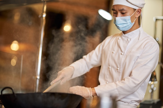 Konzentrierter männlicher Koch rührt sein Gebräu in einem Wok