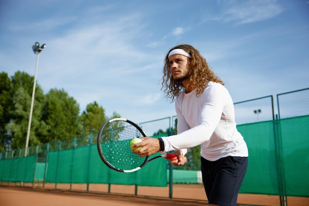 Konzentrierter männlicher Tennisspieler beim Schläger- und Balltraining auf dem Außenplatz. Vorbereitung zum Servieren