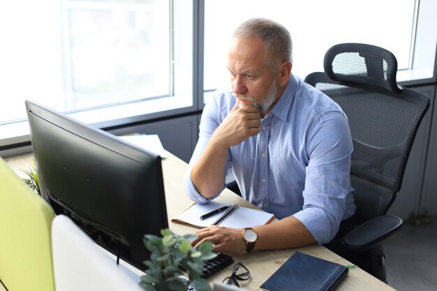 Konzentrierter reifer Geschäftsmann tief in Gedanken beim Sitzen an einem Tisch in einem modernen Büro.