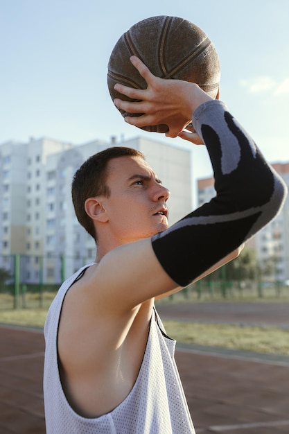 Konzentrierter Sportler in Activewear, der Basketball wirft, während er auf dem Sommerplatz Straßenball spielt