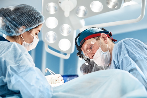 Konzentriertes chirurgisches Team, das einen Patienten in einem Operationssaal bedient. Ein gut ausgebildeter Anästhesist mit jahrelanger Ausbildung an komplexen Maschinen begleitet den Patienten während der gesamten Operation.
