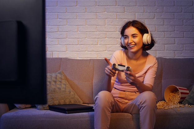 Konzentriertes, engagiertes Gamer-Mädchen, das Kopfhörer trägt und zu Hause Videospiele auf der Konsole spielt