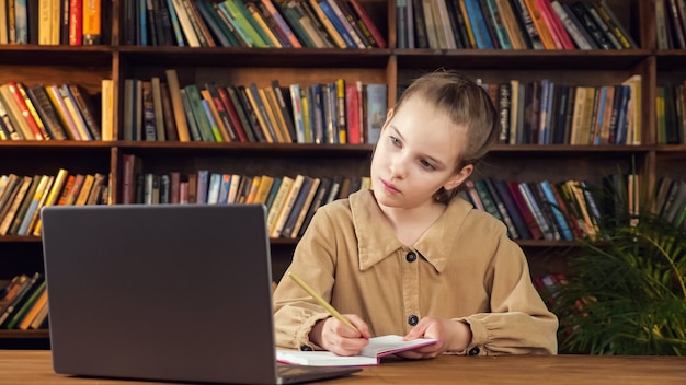 Konzentriertes Schulmädchen schaut auf Laptop-Bildschirm und schreibt
