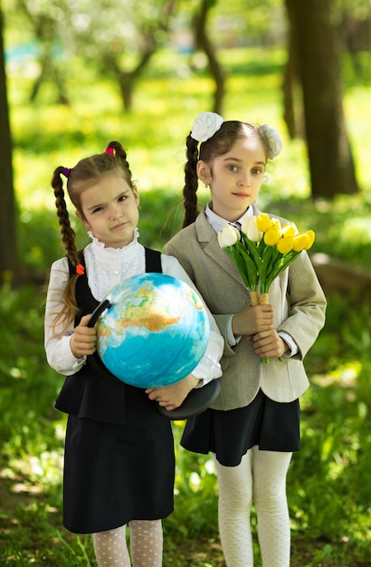 Konzept - Bildung. Zurück zur Schule. Zwei nette kaukasische Mädchenschulmädchen mit Blumen und einer Kugel, glücklich, nach Klasse in Klasse nach Hause zurückzukehren
