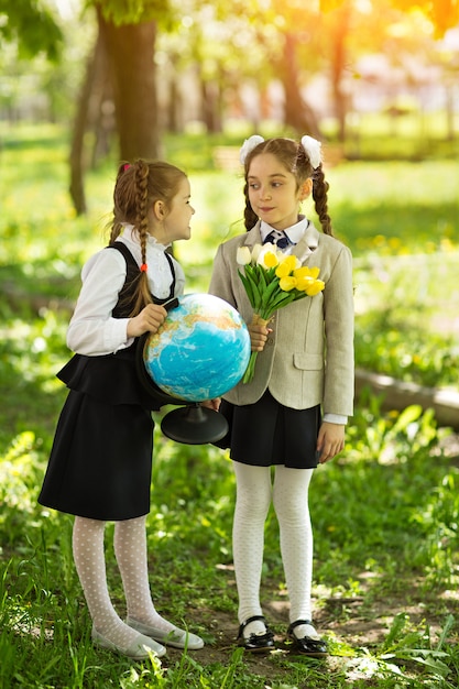 Konzept - Bildung. Zurück zur Schule. Zwei nette kaukasische Mädchenschulmädchen mit Blumen und einer Kugel, glücklich, nach Klasse in Klasse nach Hause zurückzukehren