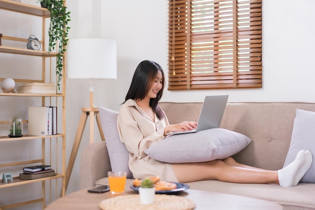 Konzept der Aktivität im Wohnzimmer Junge asiatische Frau benutzt Laptop, um auf dem Sofa in sozialen Medien zu surfen