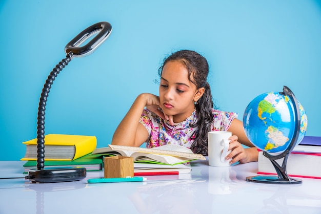 Konzept der Bildung zu Hause - Nettes kleines indisches oder asiatisches Mädchen, das zu Hause mit Bücherstapel, Bildungsglobus usw. studiert. Selektiver Fokus