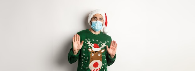 Konzept der Covid- und Weihnachtsferien ängstlicher und ausflippender Typ in Weihnachtsmütze mit medizinischer Maske rej