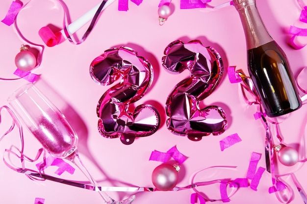 Konzept der Feiertage und des neuen Jahres 2022 rosa Folienballons Champagnerglas mit rosa Glitzer