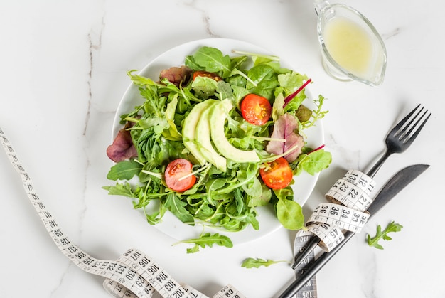 Konzept der gesunden ausgewogenen Ernährung, Gewichtsverlust, Kalorienzählung. Platte mit Blättern des grünen Salats, Tomaten, Avocado mit Joghurtbehandlung