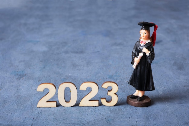 Konzept der Klasse 2023 Holznummer 2023 mit graduierter Statuette auf konkretem Hintergrund