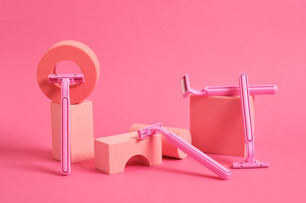 Konzept der Körperpflege von Frauen. verschiedene geometrische Stände und Podeste und mehrere rosa Rasiermesser auf rosa Hintergrund.