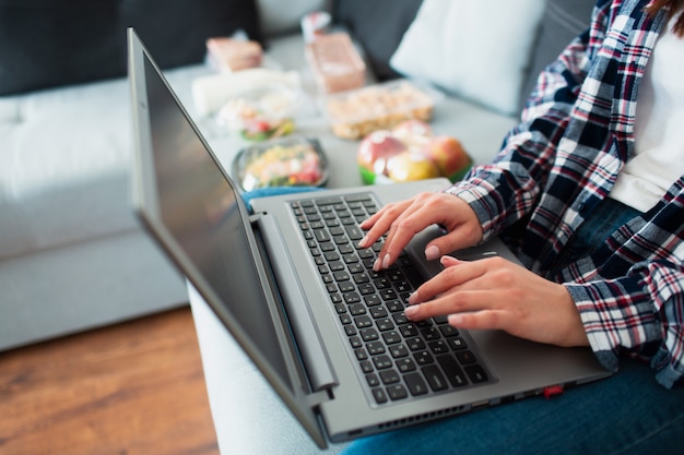 Konzept der Lebensmittellieferung. Eine junge Frau bestellt zu Hause Essen mit einem Laptop.