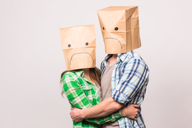 Konzept der Liebes-, Familien- und Beziehungsprobleme - unglückliches Paar, das ihre traurigen Gesichter mit Papiertüte auf weißem Hintergrund bedeckt.