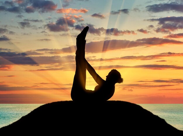 Konzept der Meditation und Entspannung. Silhouette eines Mädchens, das Yoga-Kurse auf dem Hintergrund des Sonnenuntergangs am Meer praktiziert