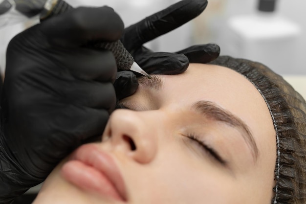 Konzept der Microblading-Augenbrauen Die Kosmetikerin führt das Verfahren des Permanent Make-up durch