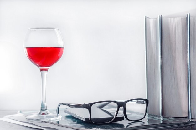 Konzept der Online-Bildung, Heimstudium. Auf dem Tisch steht ein Glas Rotwein, eine Reihe Bücher, Gläser, ein Smartphone und eine Arbeitsmappe.