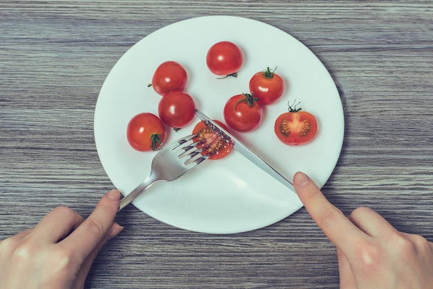 Konzept der strengen Diät. Frauenhände schneiden kleine Kirschtomate auf großem Teller