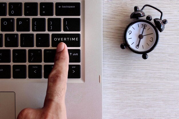 Foto konzept der überstundenarbeit fingerdruck auf der tastatur mit text überzeiten und schwarzem wecker