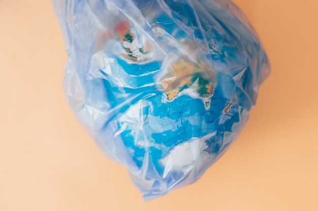 Konzept der Verschmutzung der Erde. Globus in enger Plastiktüte auf Orange