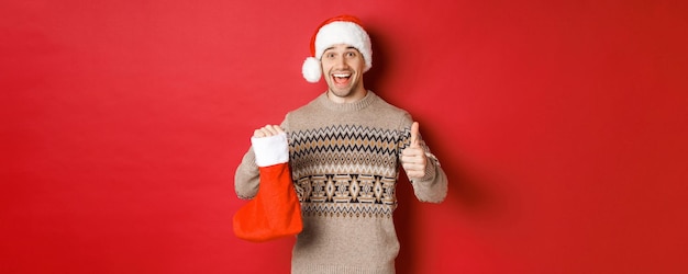 Konzept der winterferien neujahr und feier fröhlicher gutaussehender mann in weihnachtsmütze und pullover s...