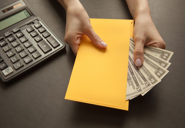 Konzept des Empfangens des Gehaltes in einem Umschlag. Gelber Umschlag mit Geld auf einer dunklen Tabelle.