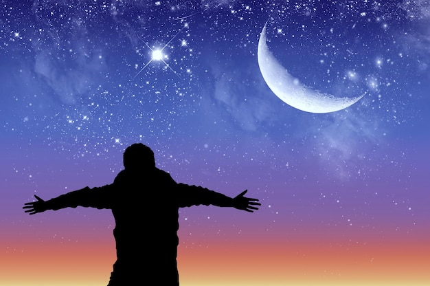 Konzept des Erfolgs. Silhouette eines glücklichen Mannes auf dem Hintergrund des Sternenhimmels und des Mondes