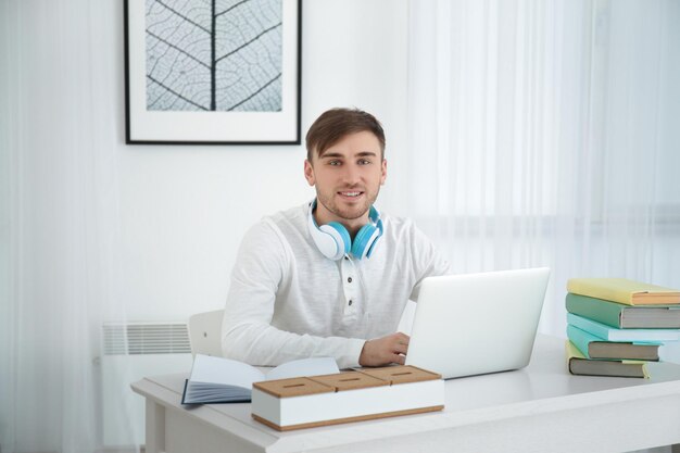 Konzept des Hörbuchs Schöner junger Mann mit Kopfhörern und Laptop am Tisch sitzen