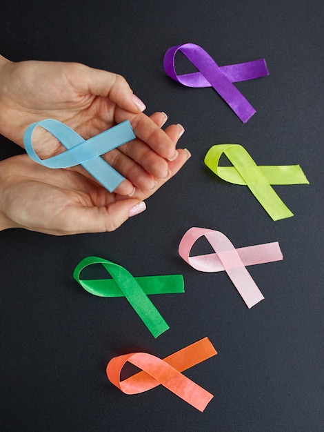 Konzept des Internationalen Brustkrebs-Bewusstseinsmonats Frau hält die Hände mit einem blauen Band auf dunkel isoliert
