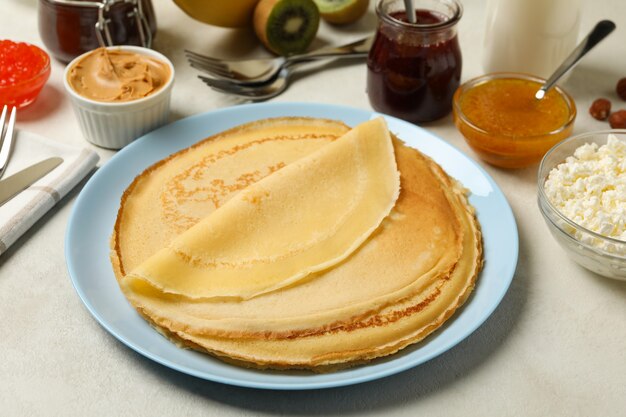 Konzept des Kochens des Frühstücks mit dünnen Pfannkuchen und Zutaten auf weißem strukturiertem Hintergrund