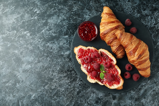 Konzept des köstlichen Essens mit Croissants mit Himbeermarmelade auf schwarzem Rauchhintergrund