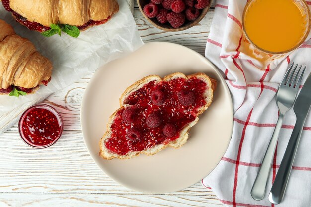 Konzept des köstlichen Essens mit Croissants mit Himbeermarmelade auf weißem Holzhintergrund