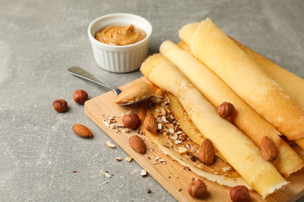 Konzept des köstlichen Frühstücks mit Crepes mit Erdnussbutter und Nüssen auf grauem Tisch