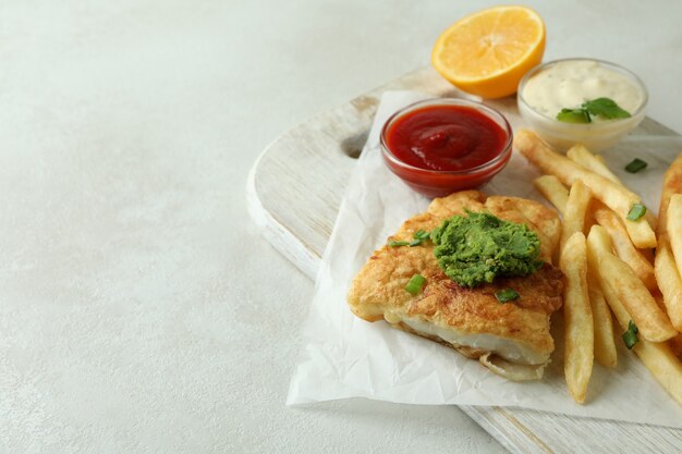 Konzept des leckeren Essens mit gebratenem Fisch und Pommes auf weiß strukturiertem Tisch