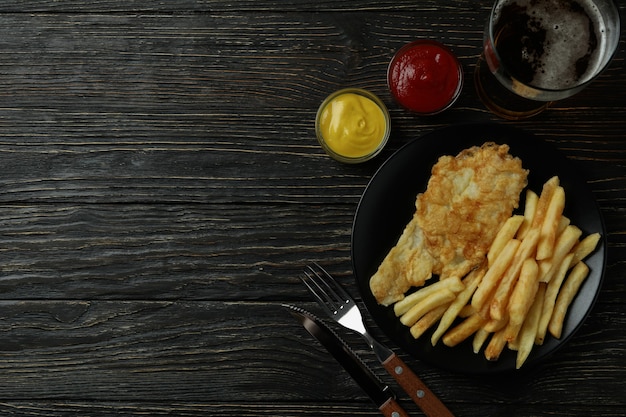 Konzept des leckeren Essens mit gebratenen Pommes und Fisch und Bier auf Holz