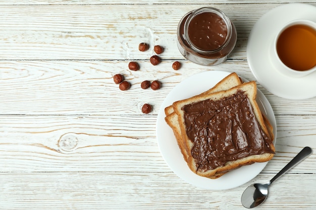 Konzept des leckeren Frühstücks mit Schokoladenpaste auf weißem Holztisch