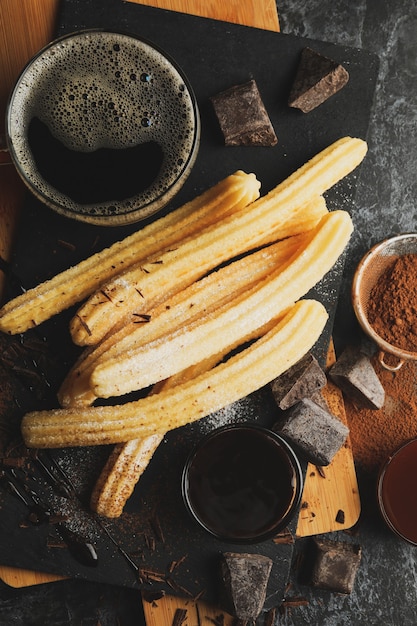 Konzept des Mittagessens mit Churros und Schokolade auf dunklem Tisch