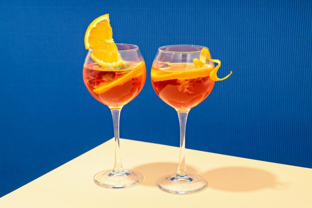 Konzept des Sommercocktails Aperol Spritz auf beigem Tisch vor blauem Hintergrund