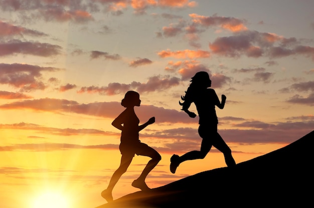 Konzept des Sports. Silhouette von zwei Mädchen, die bei Sonnenuntergang Wettbewerb laufen