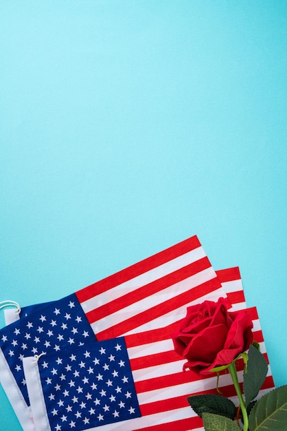 Konzept des Unabhängigkeitstages oder Memorial Day American Flag über blauem Tischhintergrund mit roter Rose