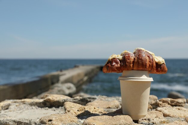 Konzept eines fantastischen Frühstücks am Meer mit Croissant und Pappbecher