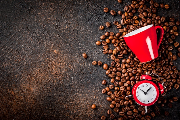 Konzept eines fröhlichen, guten starts in den tag, morgenkaffee. dunkler rostiger hintergrund mit kaffeebohnen, einem wecker und einem tasse kaffee. draufsichtkopienraum