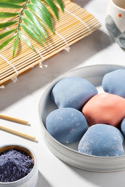 Konzept eines traditionellen japanischen Desserts auf dem Küchentisch Eine Schüssel japanischer Mochi mit Stäbchen und Holzmatte auf weißer Arbeitsplatte Asiatischer Reiskuchen Mochi-Eis Asiatisches süßes Straßenessen